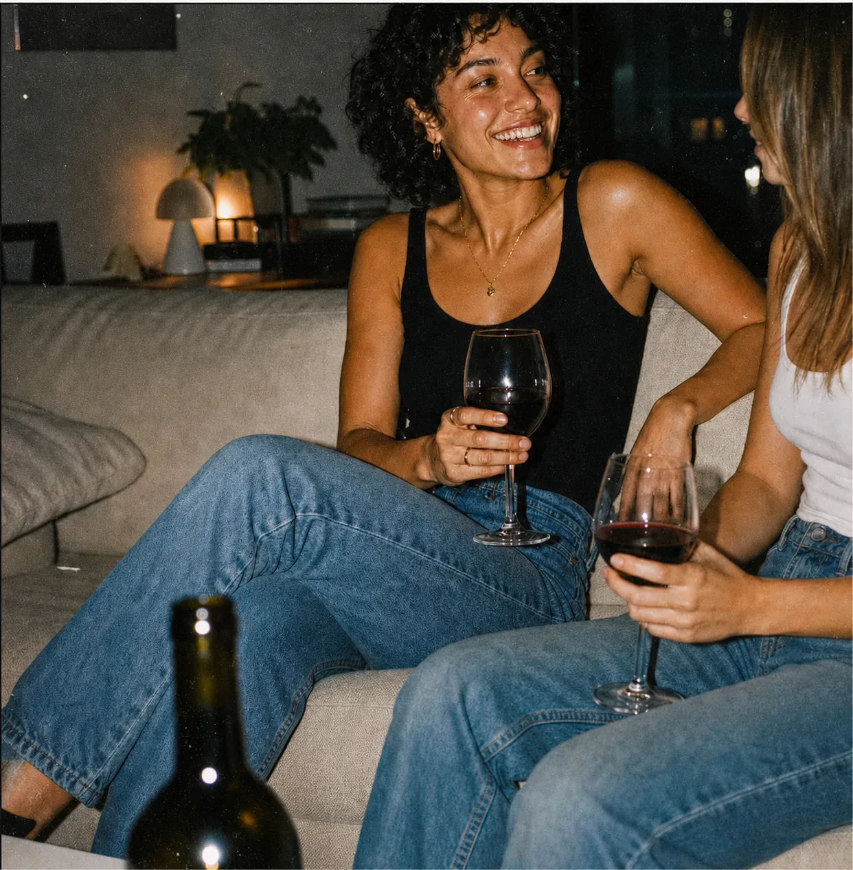 Two friends sharing red wine on a sofa at night
