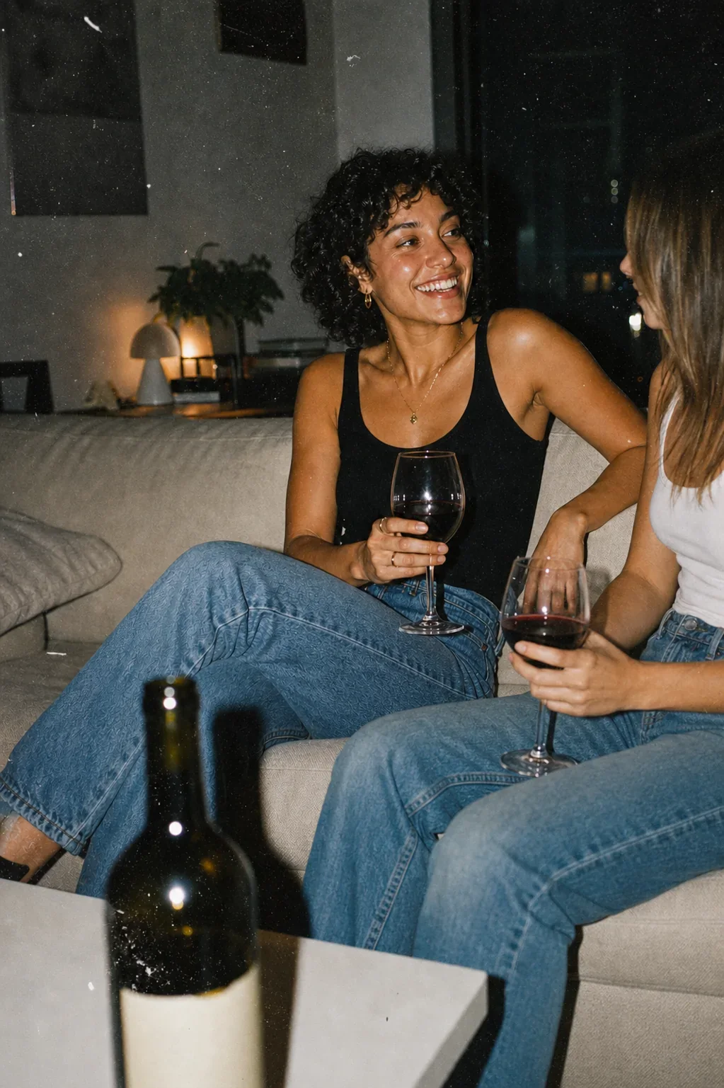 Two friends sharing red wine on a sofa at night